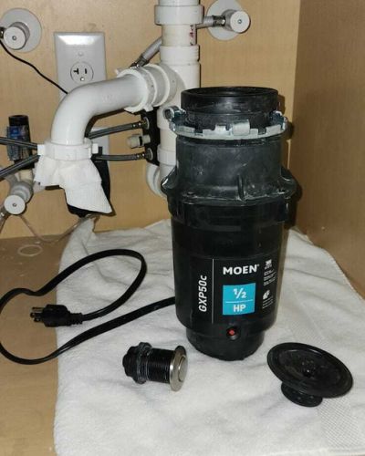 disassembled garbage disposal unit on a white towel with plumbing connections and components laid out beneath a kitchen sink