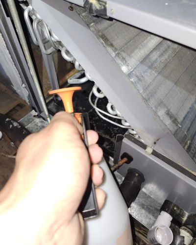 hand holding a tool spraying cleaning solution onto an air conditioning unit's components for maintenance and cleaning purposes