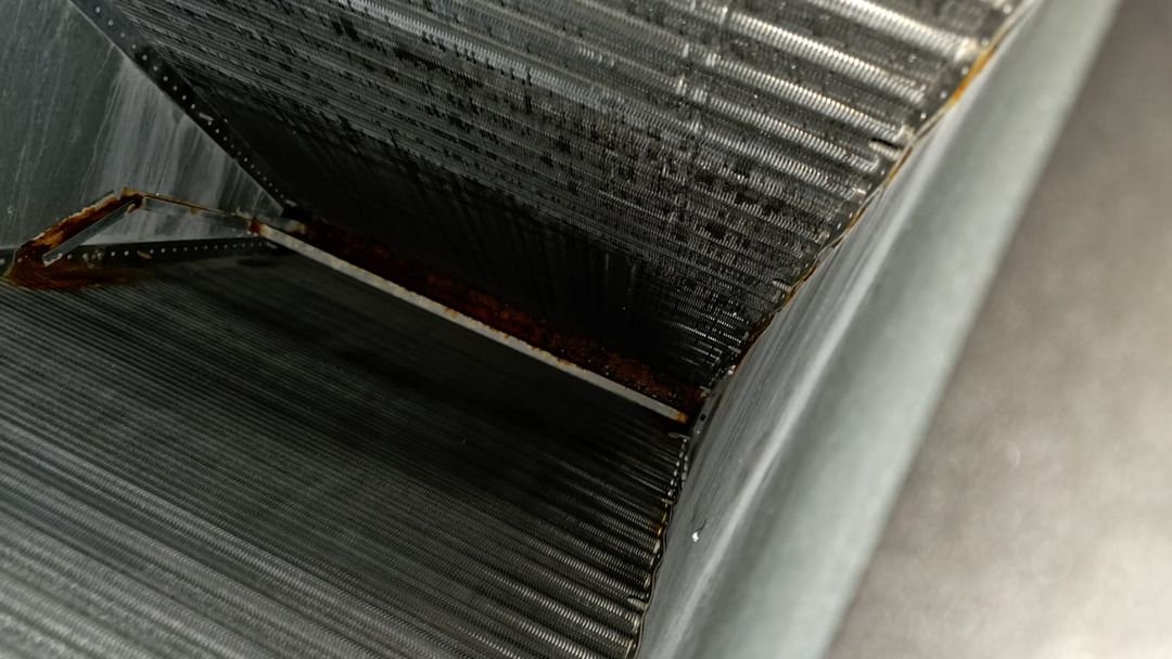 cleaning and inspecting a dirty air conditioning coil with visible rust and debris on the surface