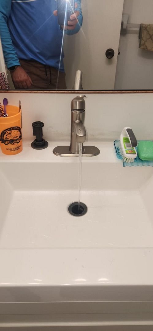 water is flowing from a modern faucet into a white sink with various toiletries on the side