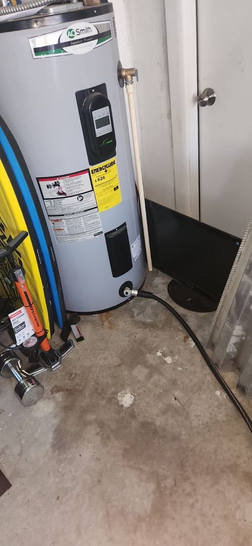 water heater installation in a garage with tools visible nearby alongside a hose and a small screen