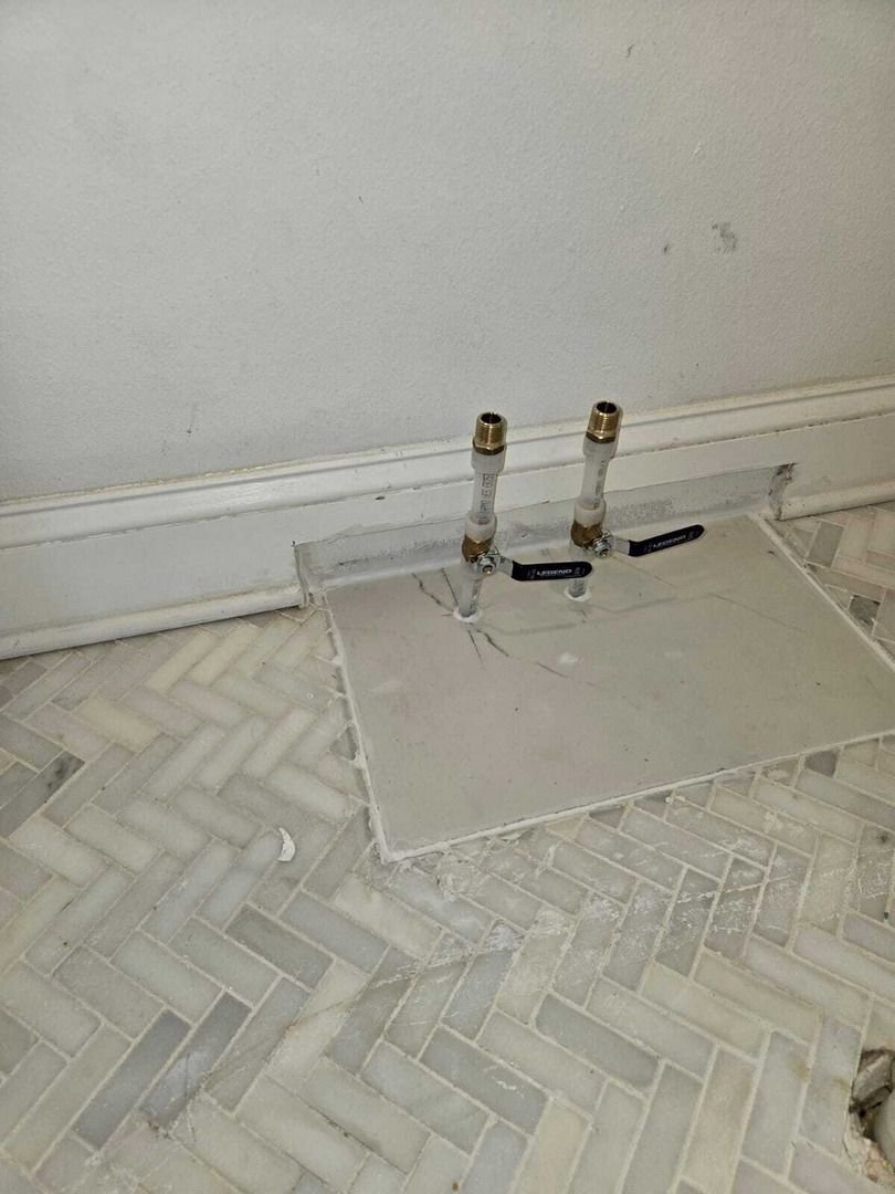 exposed plumbing valves and pipes on a tiled floor suggesting potential plumbing installation or maintenance work