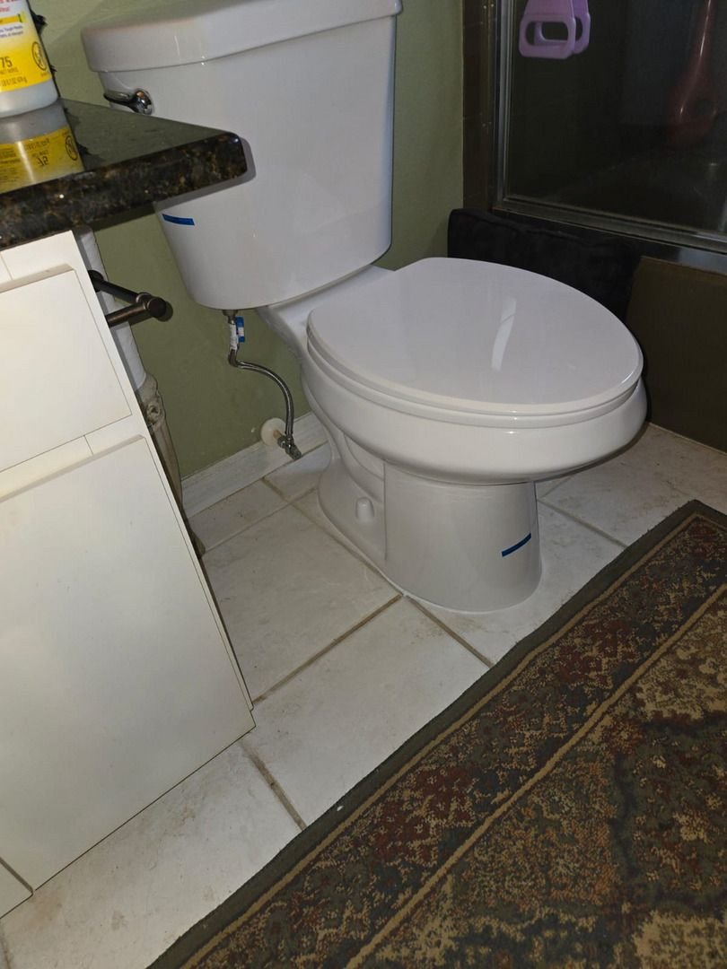 toilet installation in a bathroom with white tiles and a dark rug nearby