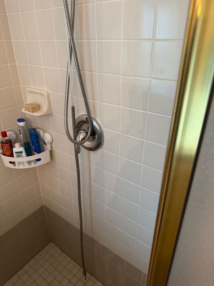 shower valve and hose installation in a tiled shower with toiletries displayed on a shower caddy