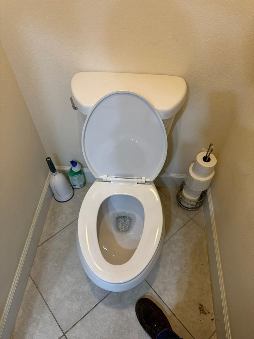 toilet installation in a bathroom with cleaning supplies and a foot seen in the lower part of the photo