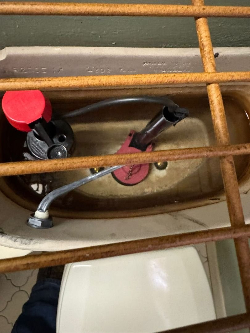 repairing a toilet tank with visible water components and red button fixture near a wooden grate