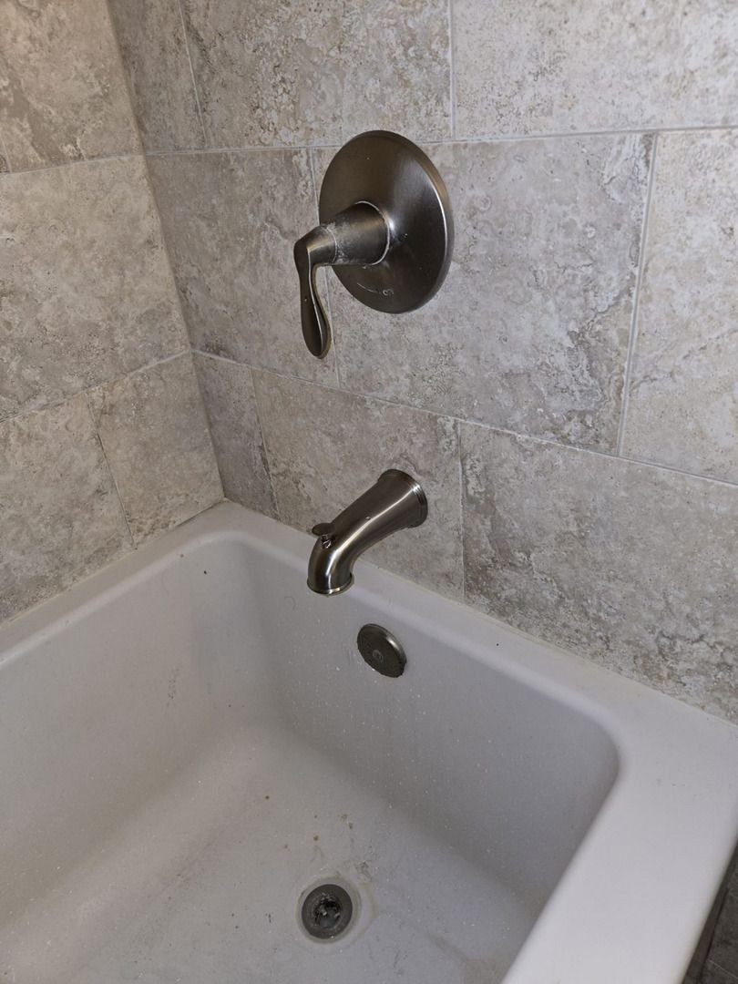 plumbing service inspecting or repairing a bathtub faucet and handle in a tiled bathroom