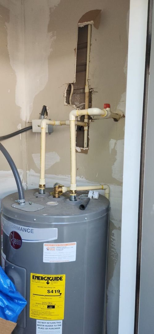 water heater installation with visible plumbing connections and energy guide label in a partially finished wall setting