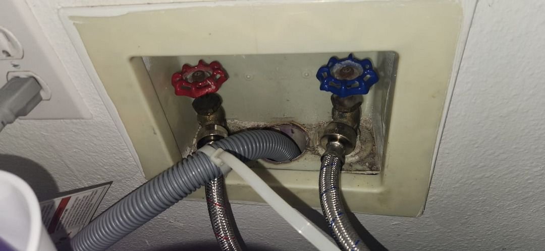 plumbing connections with blue and red valves visible alongside flexible hoses attached to a wall outlet