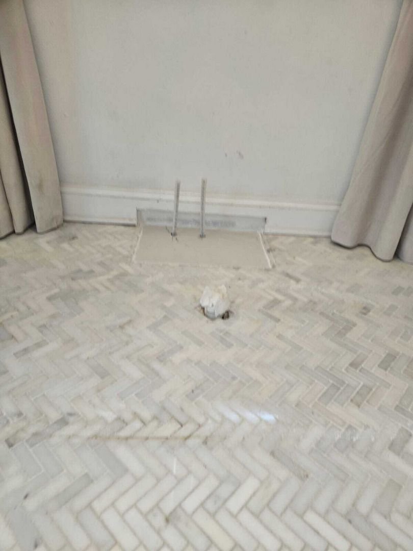 plumbing service with a floor vent and two pipes visible on a herringbone patterned tile floor