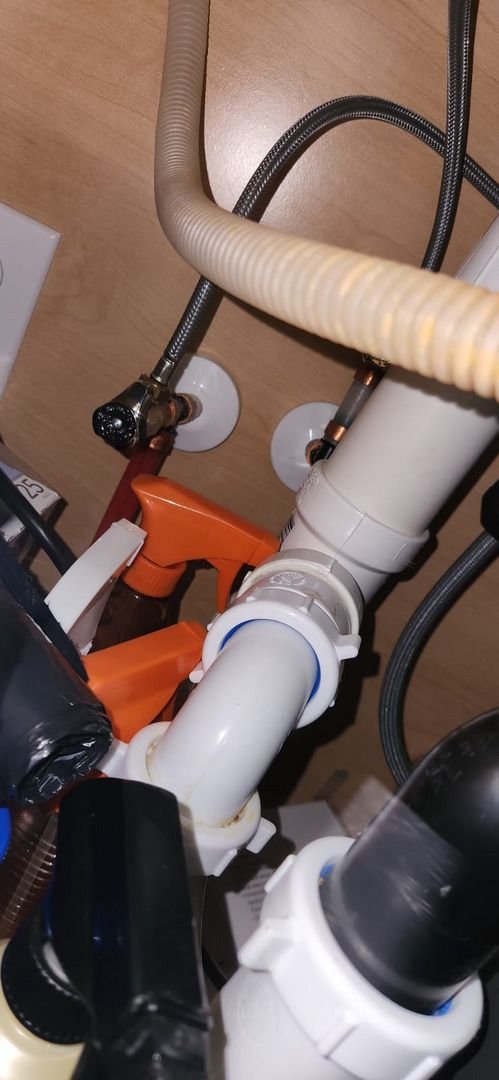 plumbing work being done under a sink featuring various pipes and valves with tools nearby for servicing