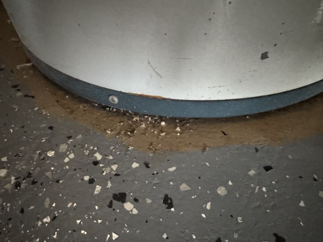 water pooling around the base of a large metal container on a concrete floor indicating a possible leak or drainage issue