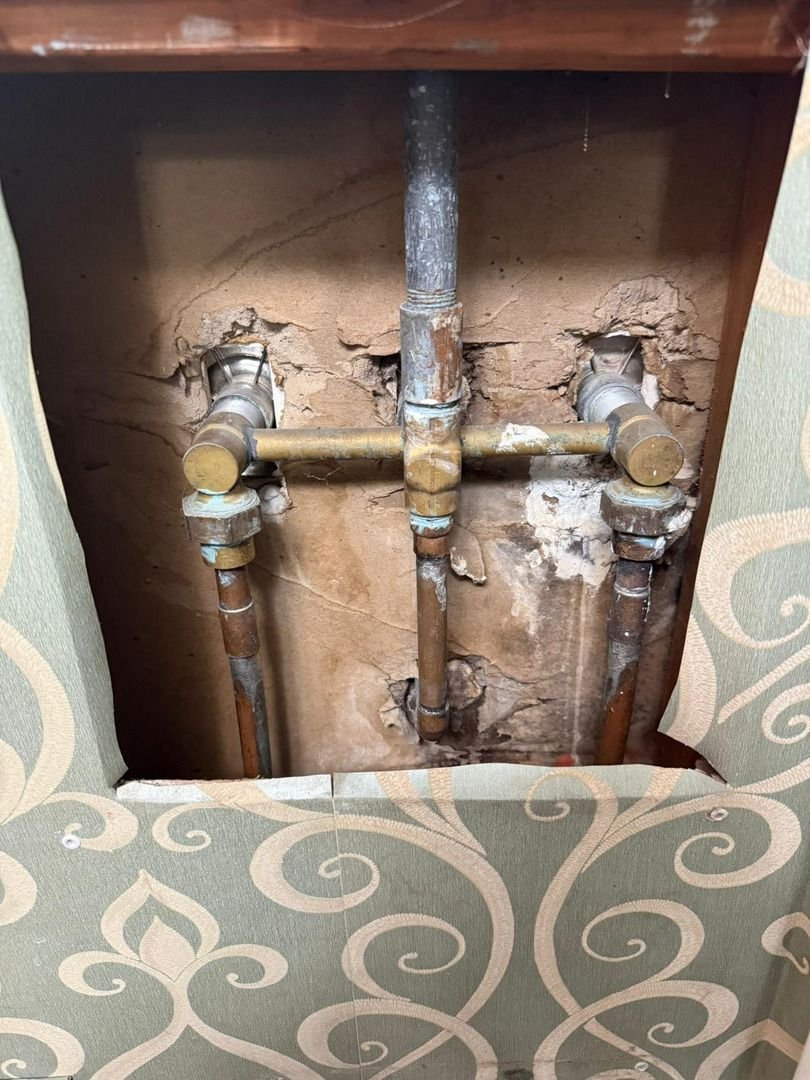 plumber repairing copper pipes behind wall with exposed fittings and damaged drywall visible