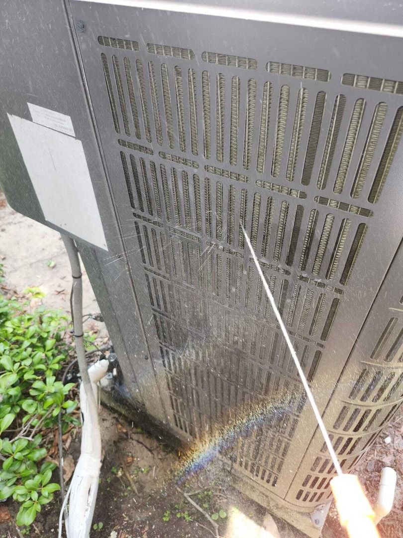 cleaning the condenser unit of an air conditioning system using a pressure washer to remove debris and dirt
