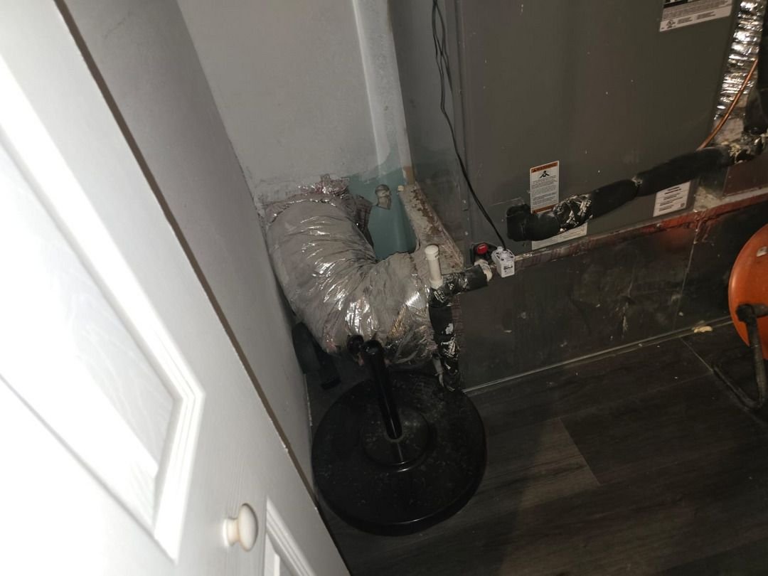 ductwork installation with insulation and plumbing connections visible in a residential setting with dark flooring