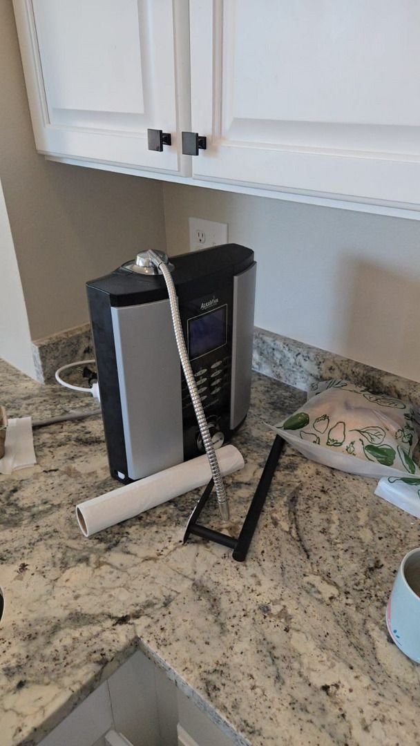 a water filtration system is set up on a kitchen countertop with a flexible hose and various objects nearby