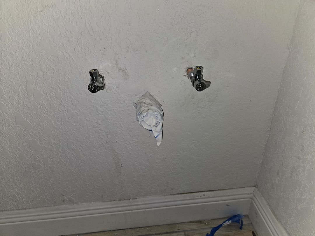 two water shutoff valves mounted on a wall with paper covering one and blue tape on the floor