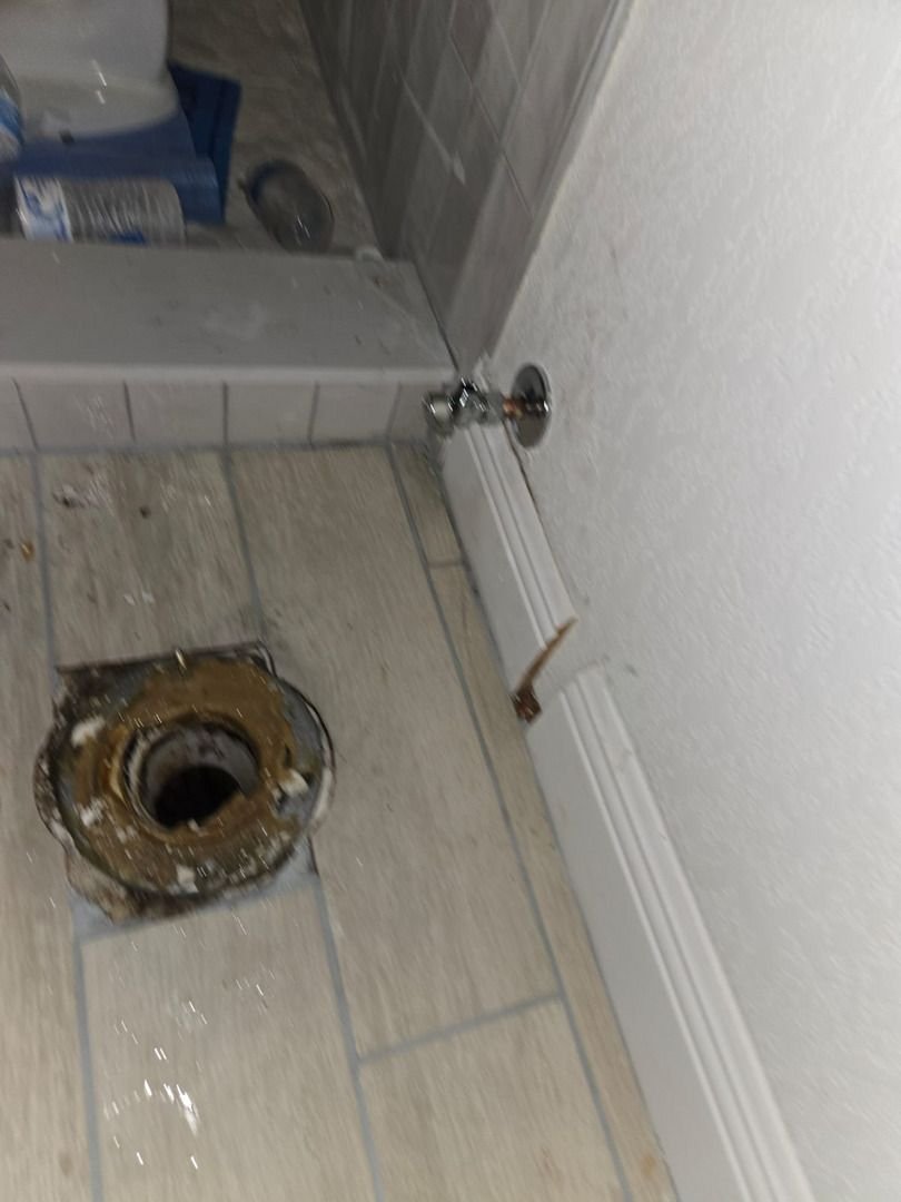 plumbing work being done with a visible toilet flange and plumbing fittings on tiled flooring