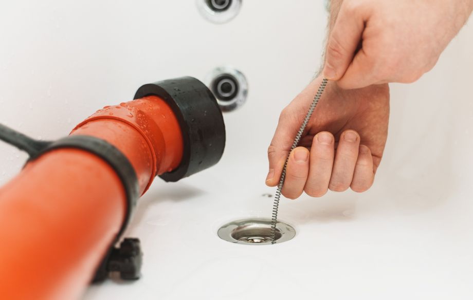 Drain Cleaning Tool In Hands With Orange Pipe And Drain