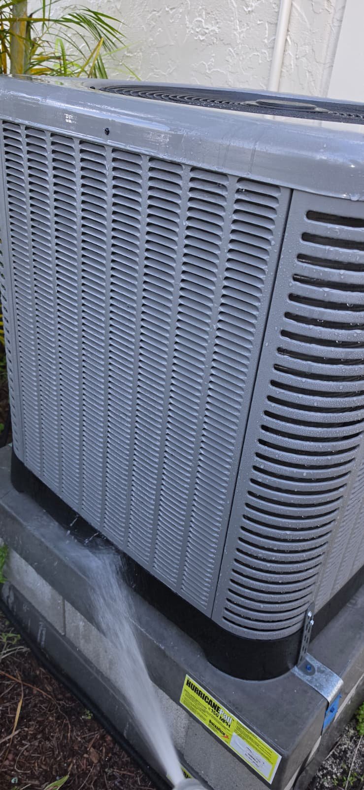 Newly installed AC unit with branding and water spray in Tampa, FL 33624. Premium Home Therapy Plan service.