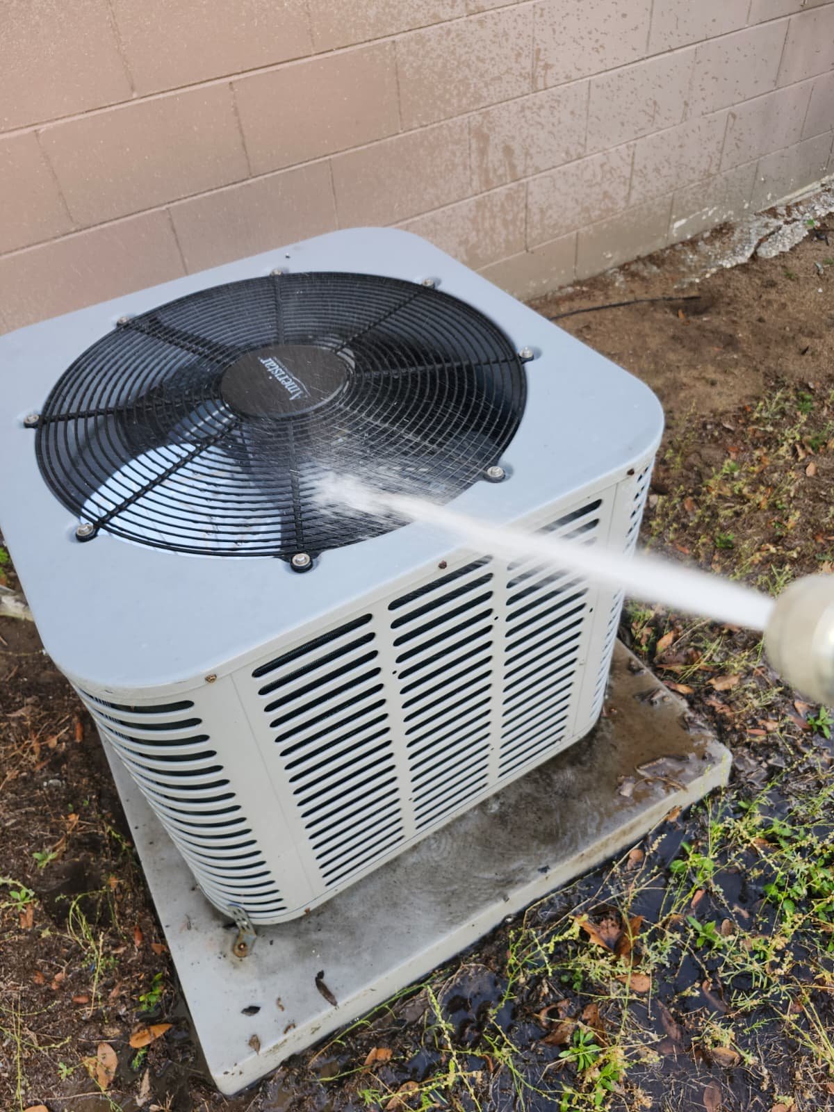 Outdoor AC unit cleaning with hose during cooling maintenance in Valrico, FL 33594.