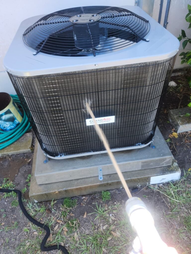 Rinsing a GrandAire condenser coil during a cleaning in Belleair Bluffs, FL 33770.