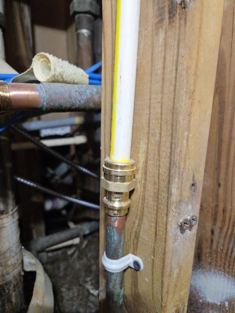 A white supply pipe joined to older copper with a brass fitting at a wall stud in Tampa, FL 33613.