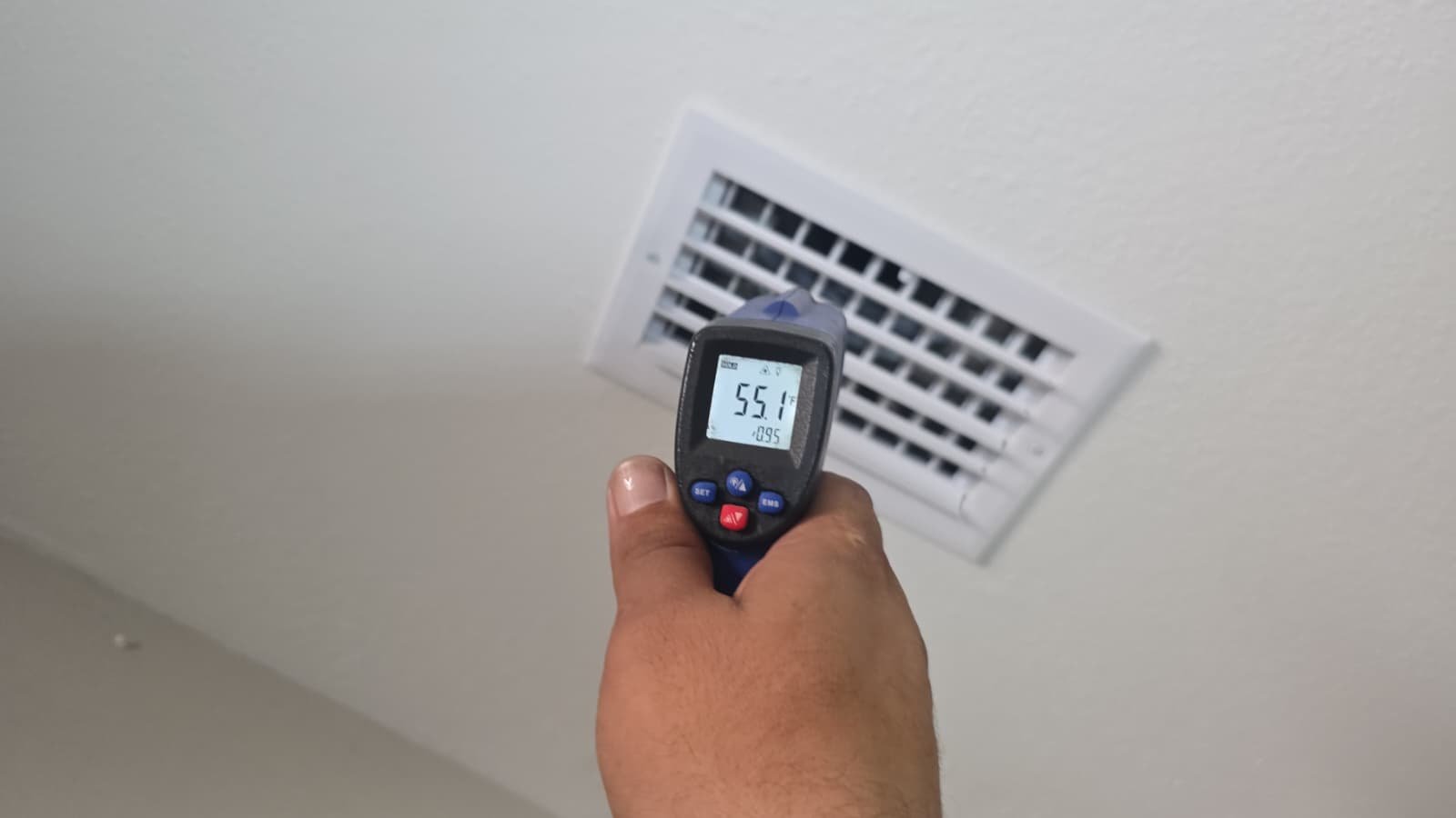Hand holding a temperature gun near an air vent showing temperature reading in Tampa, FL 33610.