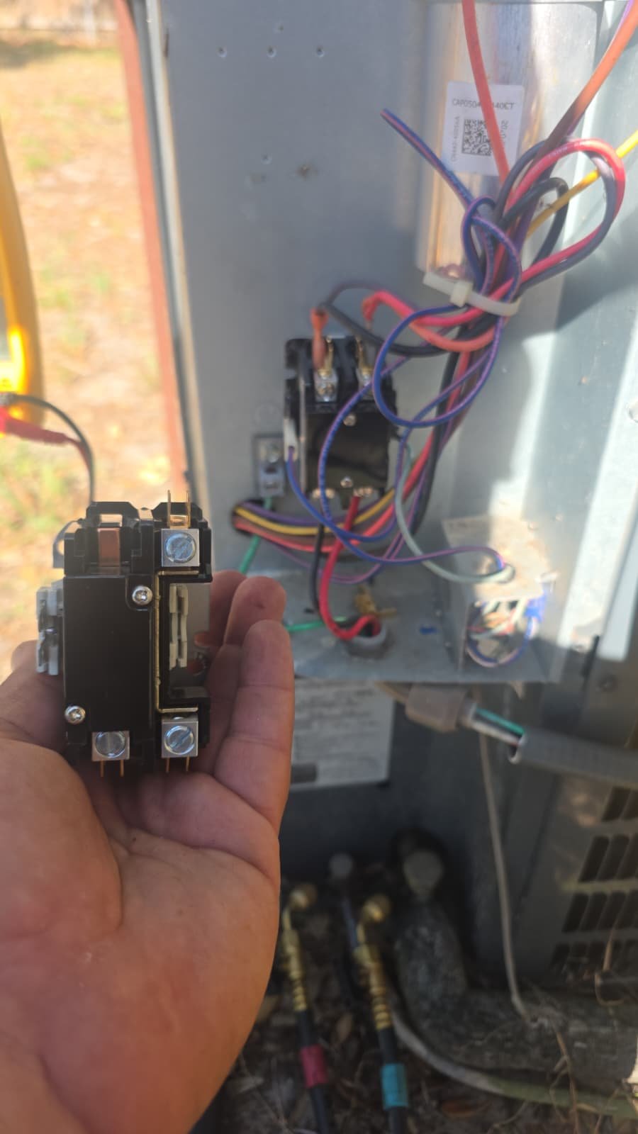 Hand holding a contactor next to wiring inside AC unit in Tampa, FL 33611.