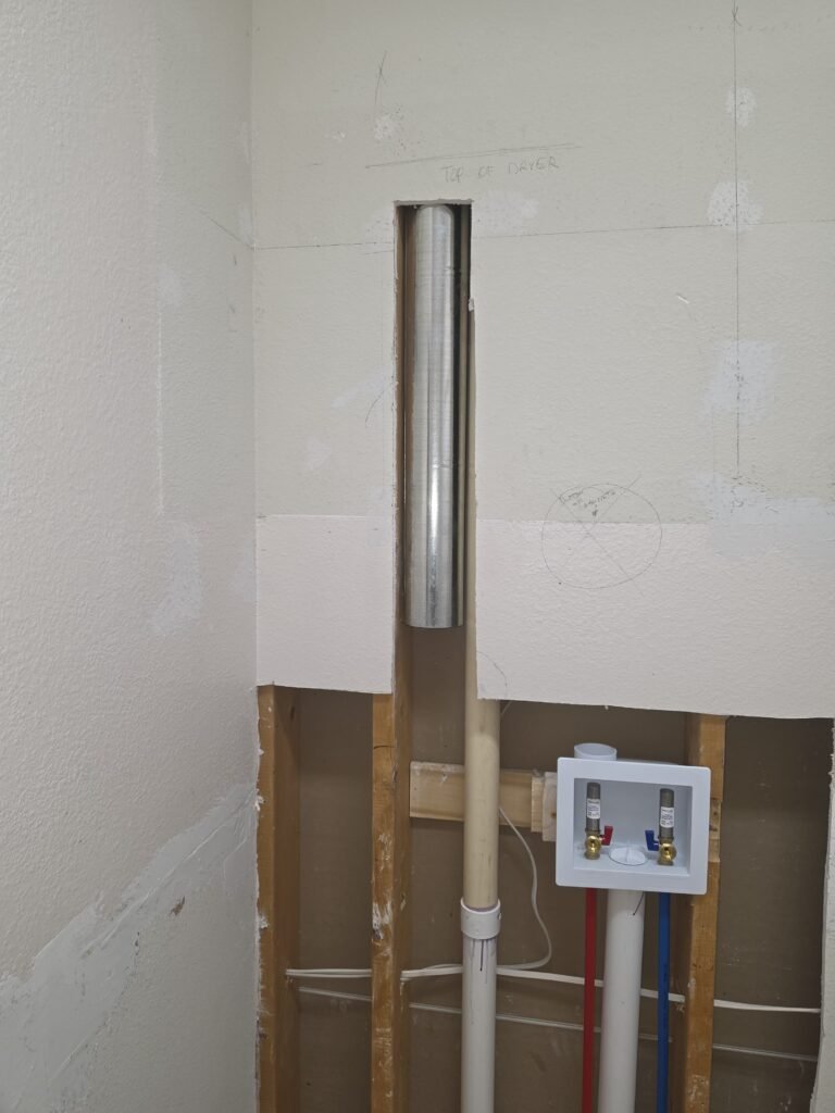 A new rigid metal dryer duct running up an open laundry room wall in Tampa, FL 33647.