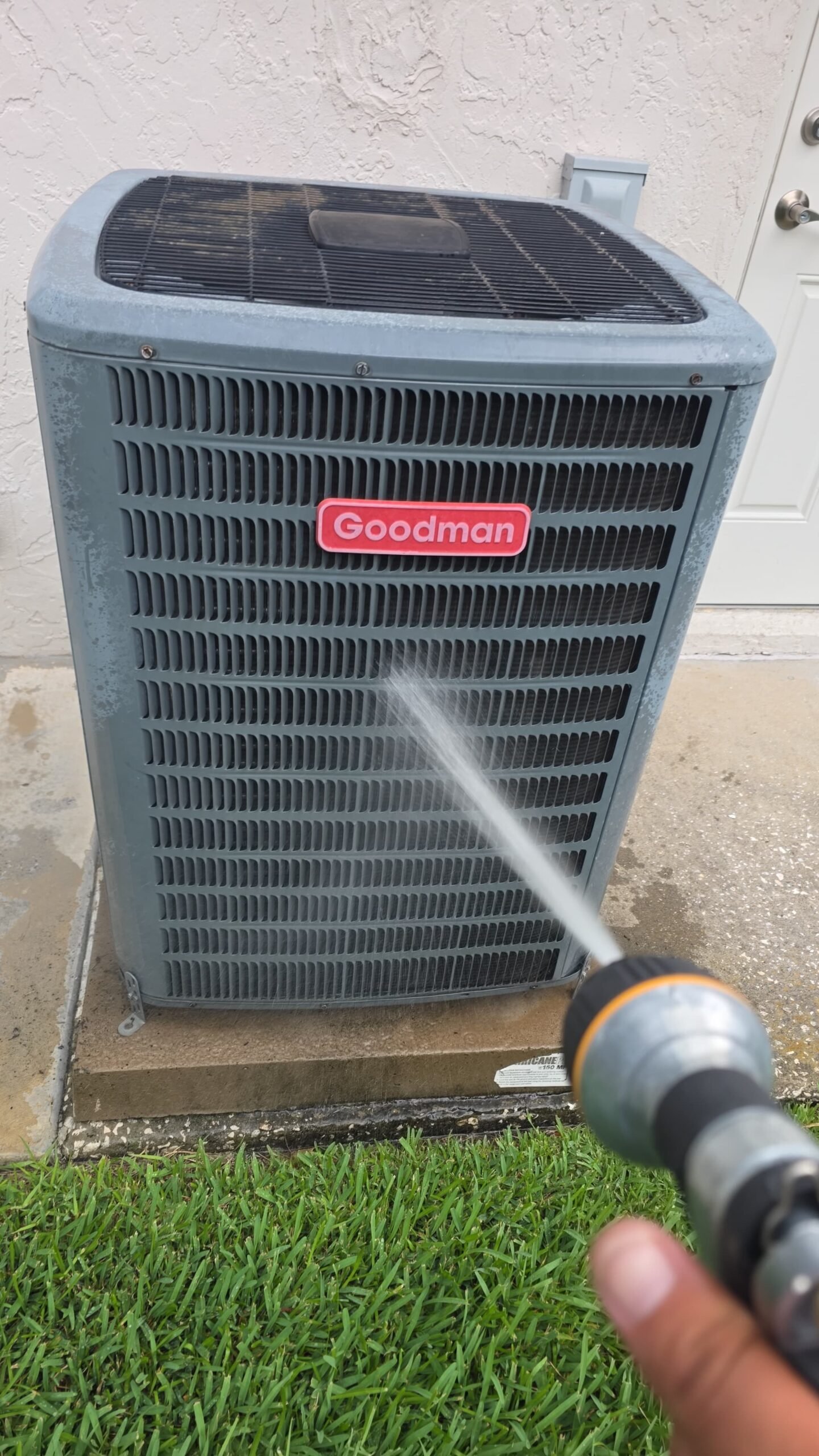 Technician cleaning Goodman AC unit with water hose in Palm Harbor, FL 34684 during Premium Therapy Plan 2.0.