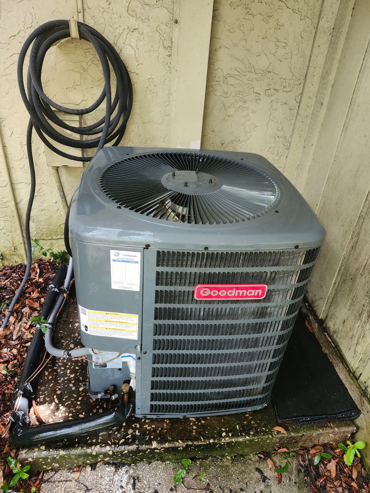 Goodman AC unit installed outside house with coiled hose in Lutz, FL 33559. Efficient cooling solution.