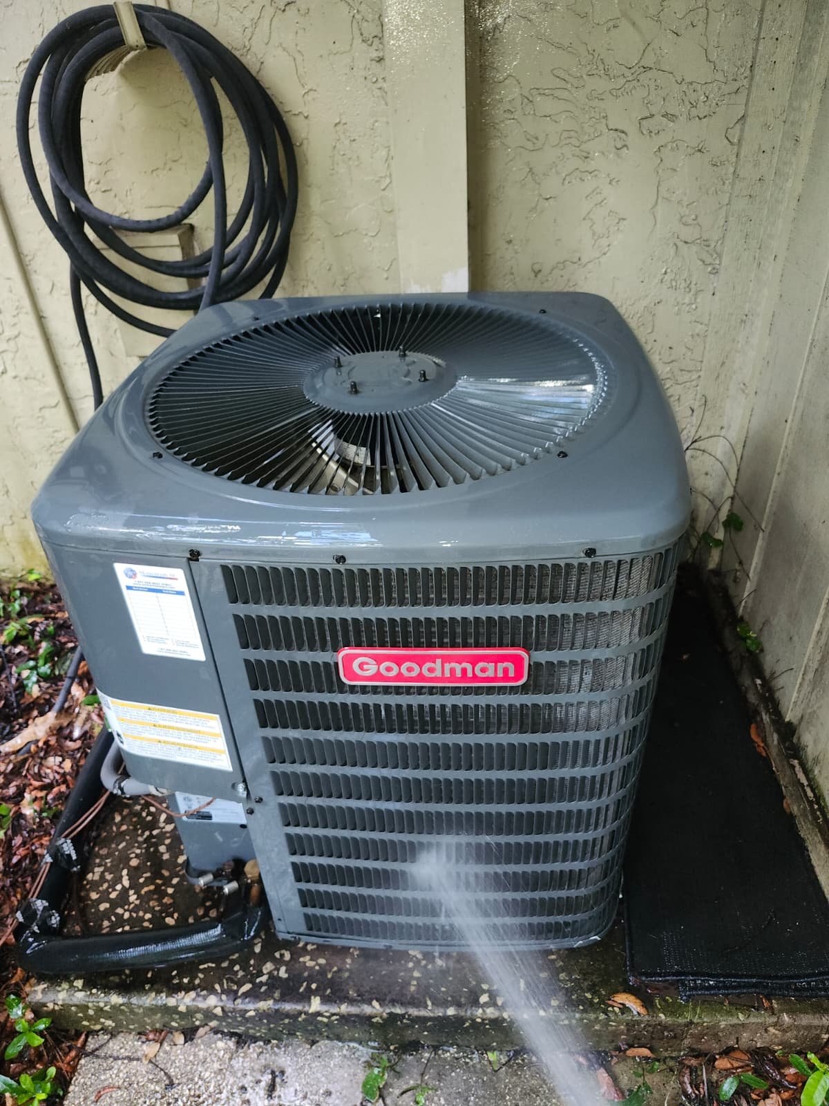 Cleaned Goodman AC unit with visible water spray in Lutz, FL 33559. Post-maintenance shine.