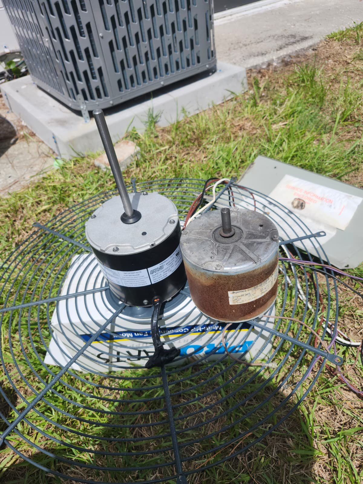 Old and new condenser fan motors placed on grass in St. Petersburg, FL 33712.