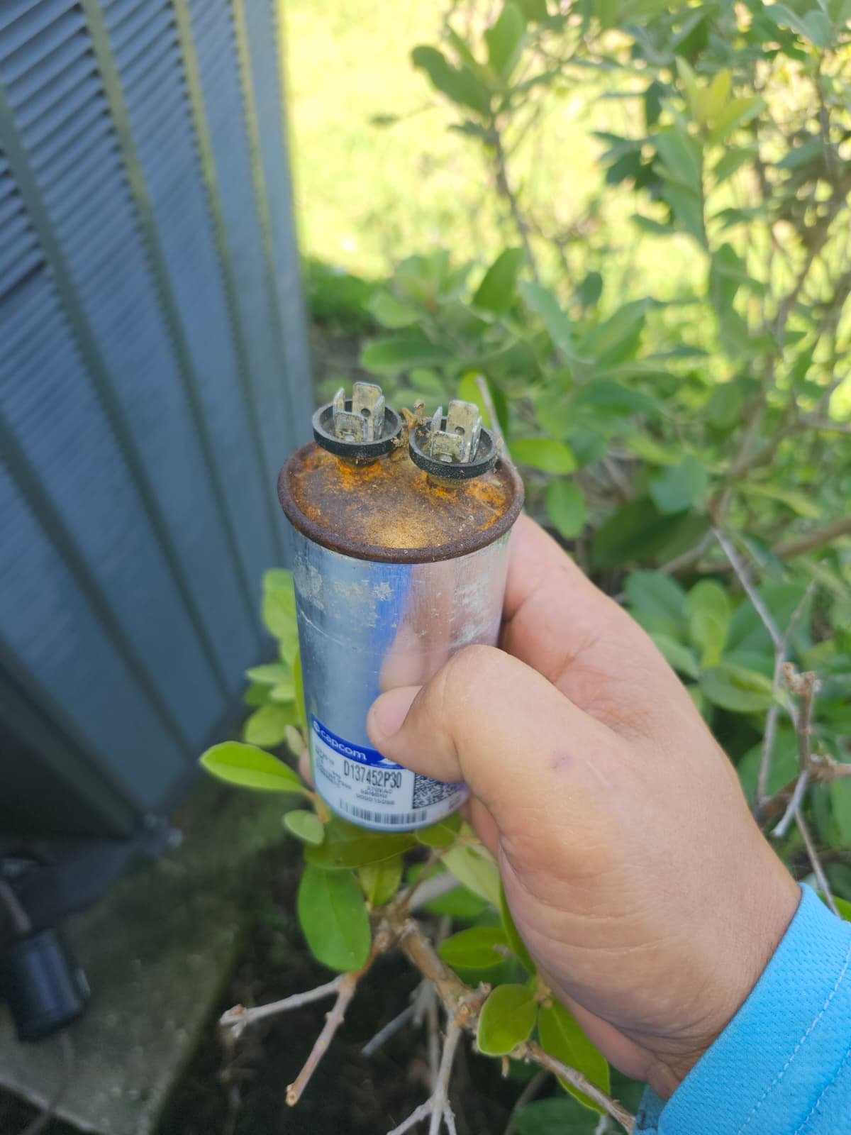 Rusty Capacitor in Parrish, FL 34219 Hand holding a rusty capacitor in front of an HVAC unit in Parrish, FL 34219.
