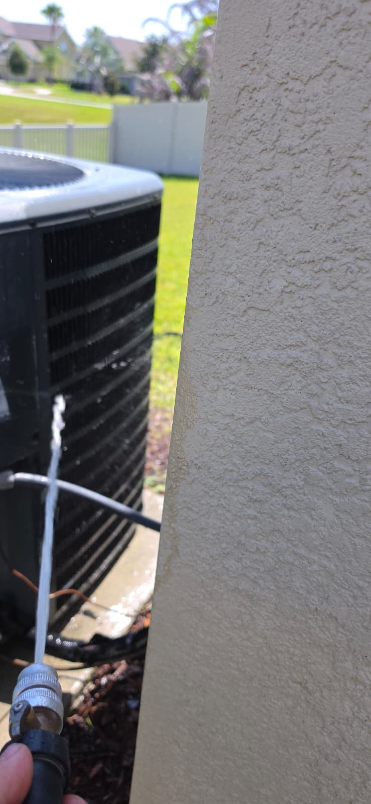 Technician cleaning outdoor AC unit with hose in Riverview, FL 33579.