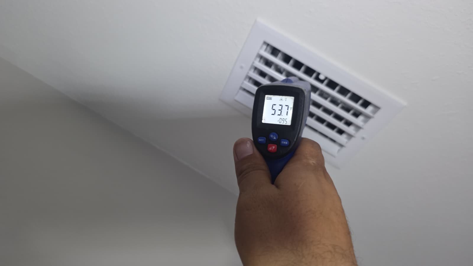 Hand holding a temperature gun near an air vent showing temperature reading in Tampa, FL 33610.