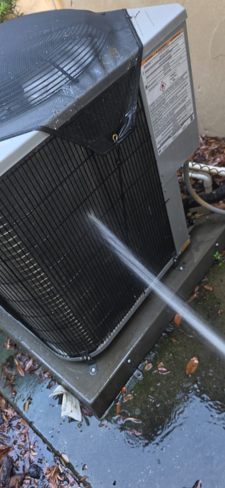 AC unit cleaning with water spray, wet ground visible, in Lutz, FL 33559.