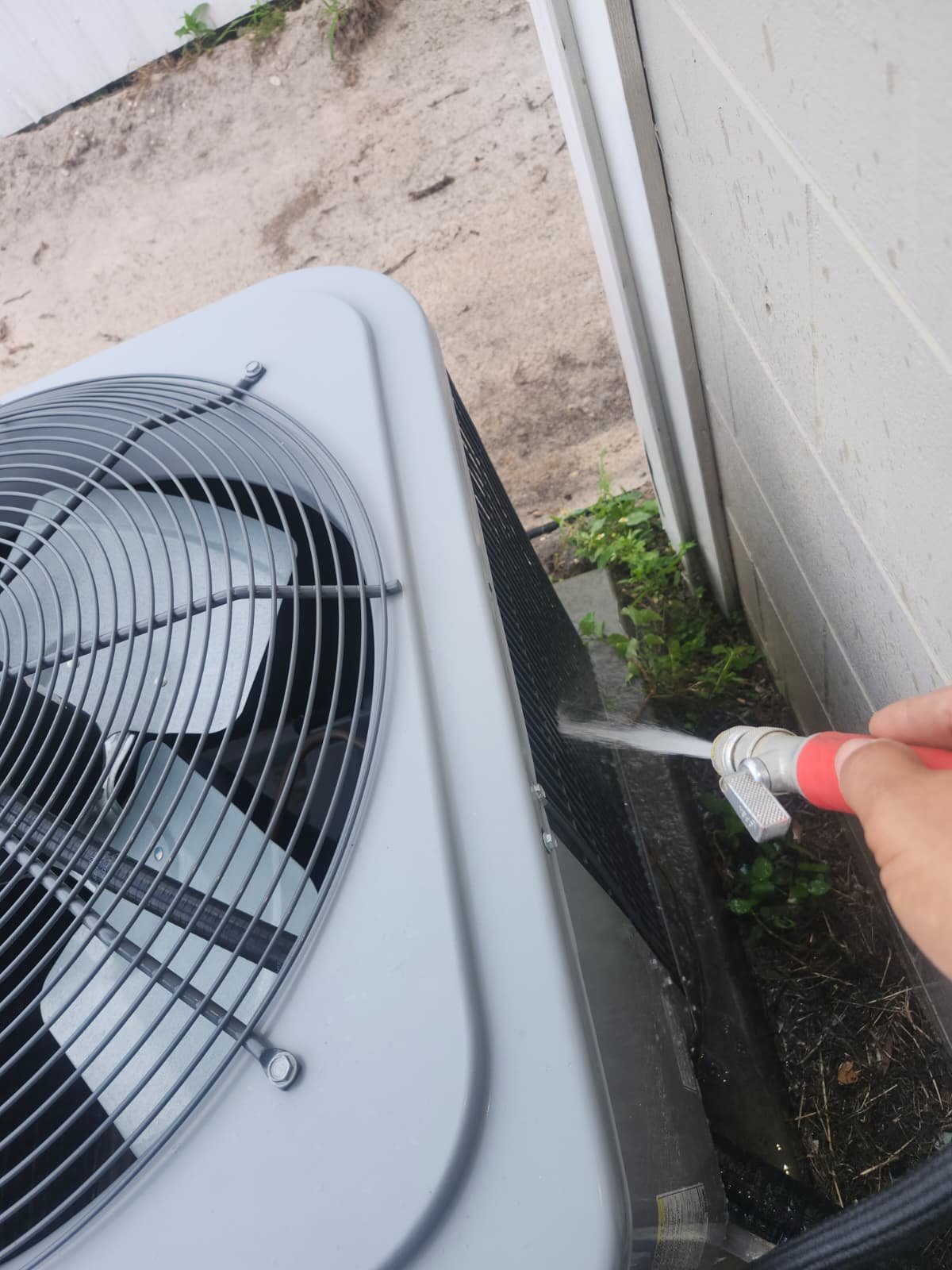 AC Cleaning Process - Tampa, FL 33614 Person cleaning an outdoor AC unit with a hose in Tampa, FL 33614. In-progress service.