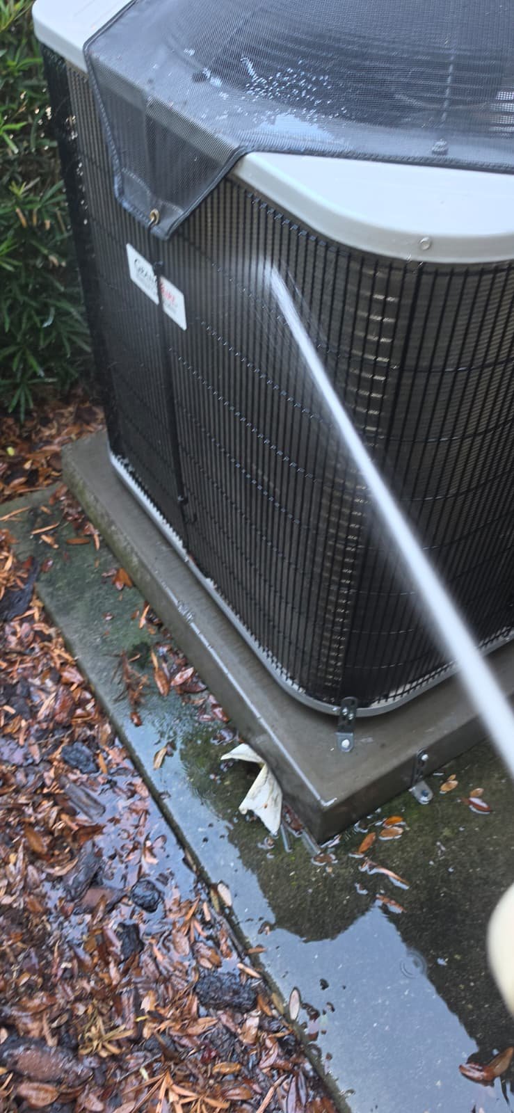 AC unit cleaning with water spray, surrounded by leaves, in Lutz, FL 33559.