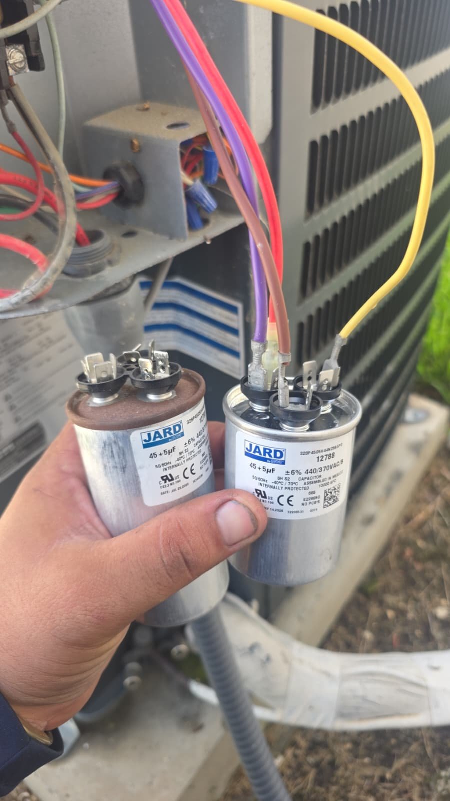 Comparison of old and new capacitors in front of AC unit, Tampa, FL 33618.
