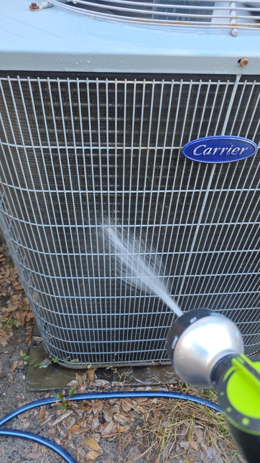 Cleaning process of outdoor Carrier AC unit with hose during Premium Therapy Plan in Tarpon Springs, FL 34689.