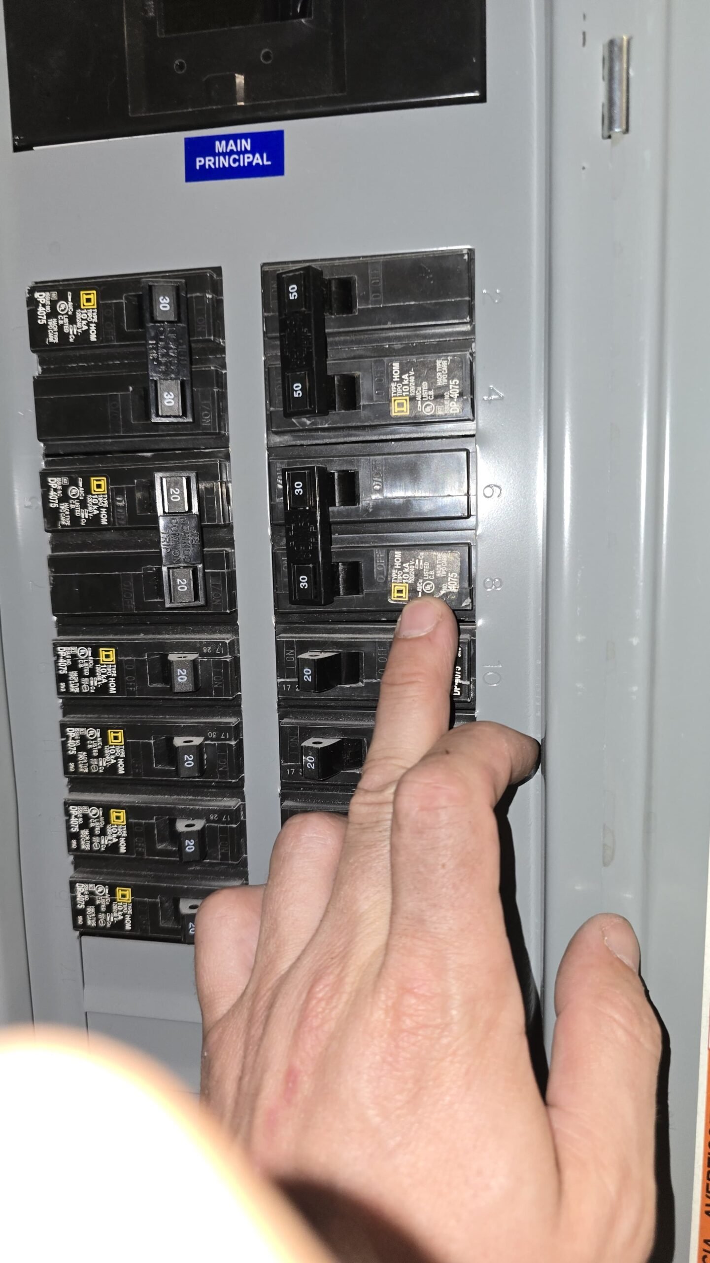 Hand pointing at circuit breaker in Tampa, FL 33613 electrical panel.