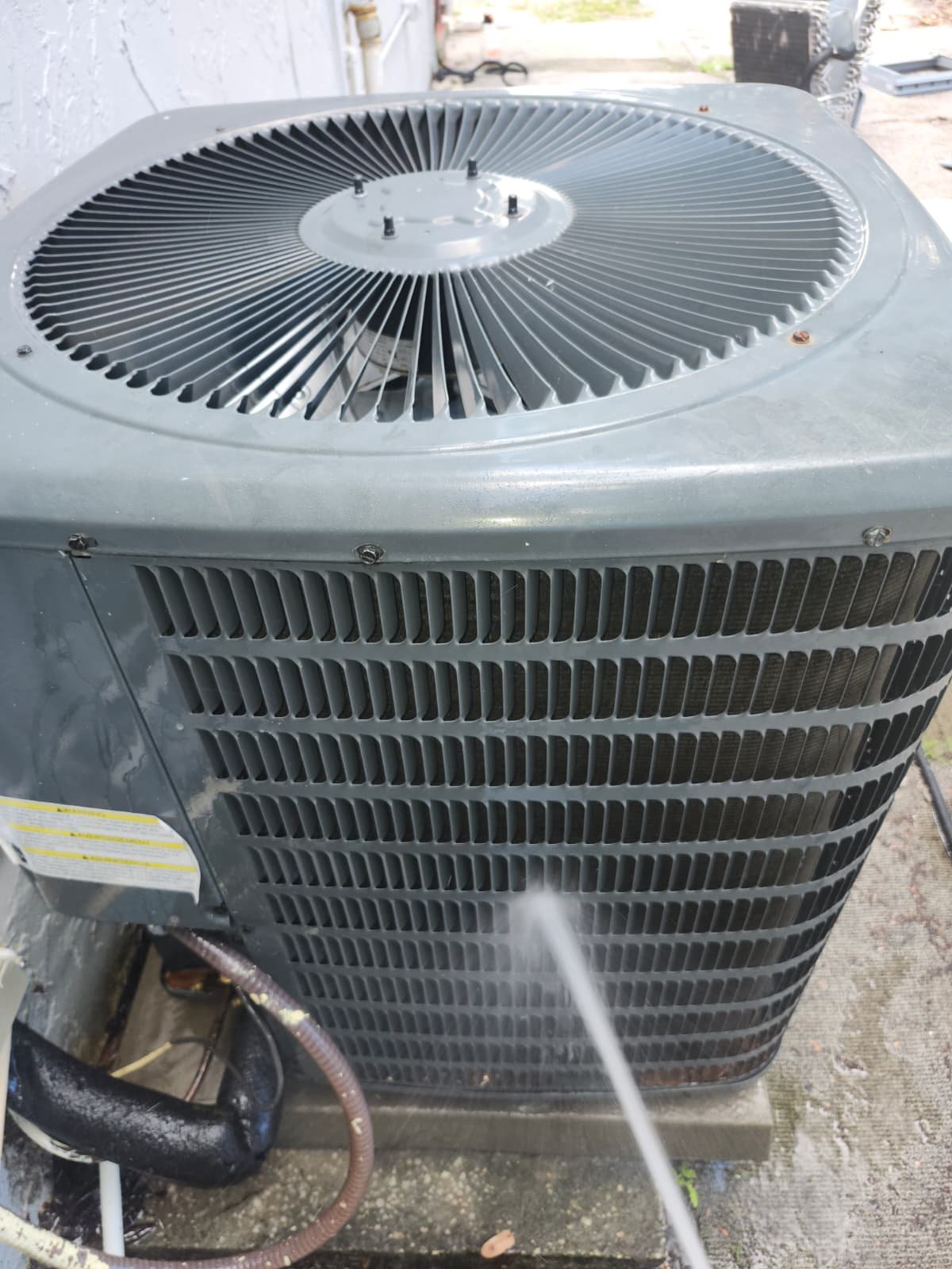 Outdoor AC unit being cleaned with water spray in Tampa, FL 33607.