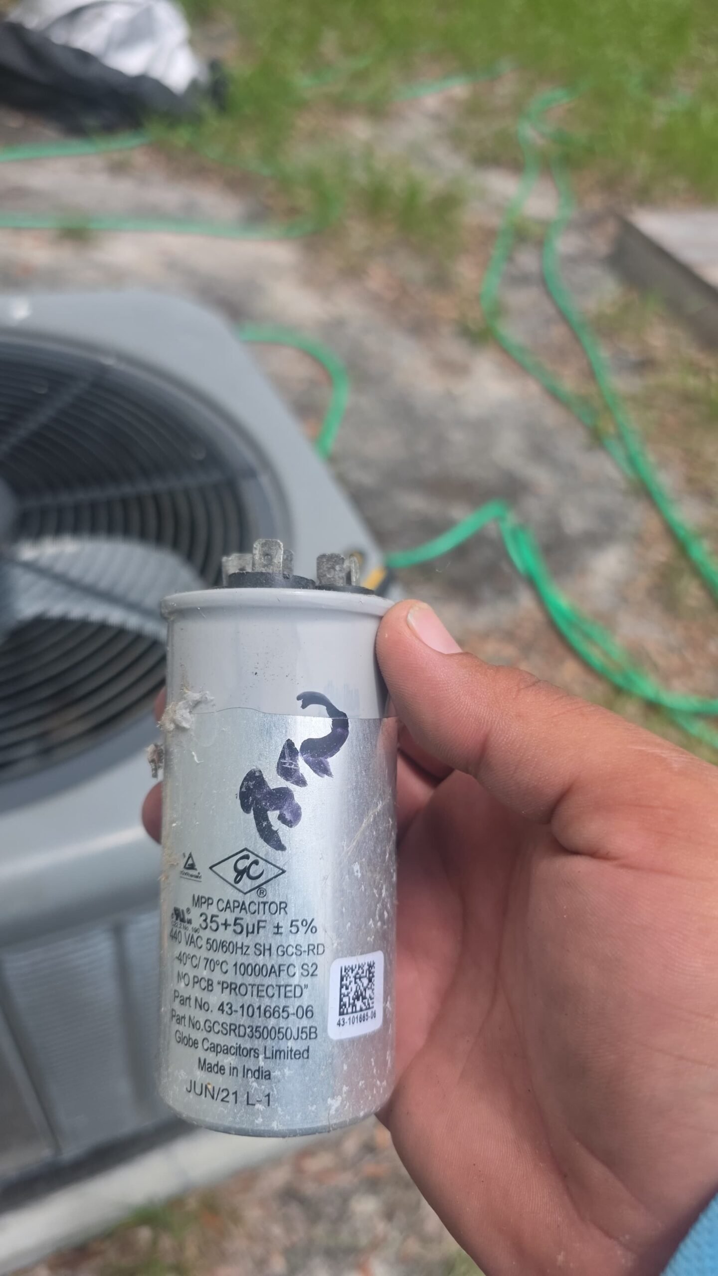 Technician holding capacitor near HVAC unit, Largo, FL 33774.