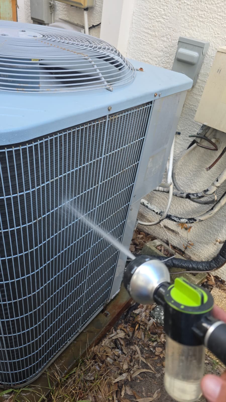Cleaning outdoor AC unit with hose nozzle during Premium Therapy Plan in Tarpon Springs, FL 34689.