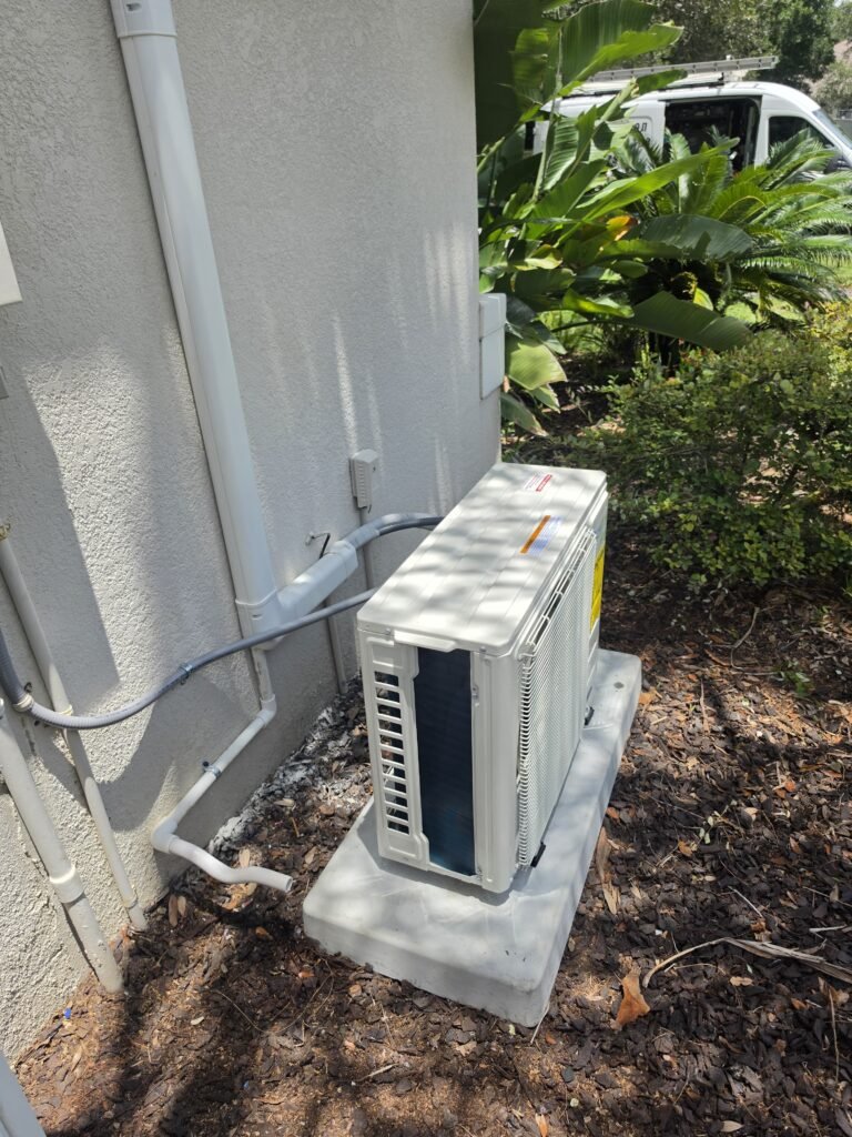 A mini split outdoor unit on its pad with the line set cover running up the wall in Lutz, FL 33558.