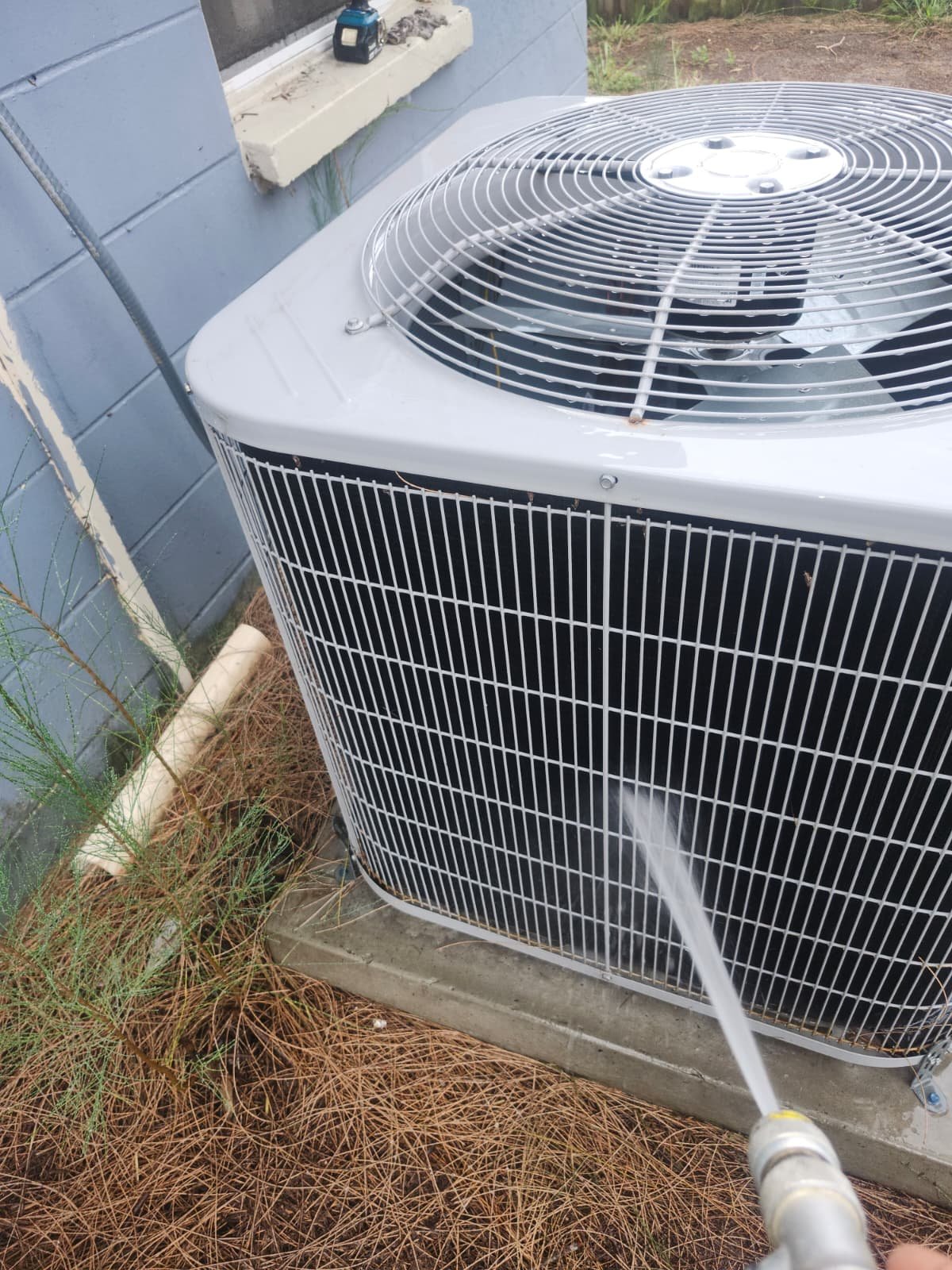 Cleaning an outdoor AC unit with a hose after Visit #3 in Tampa, FL 33619.
