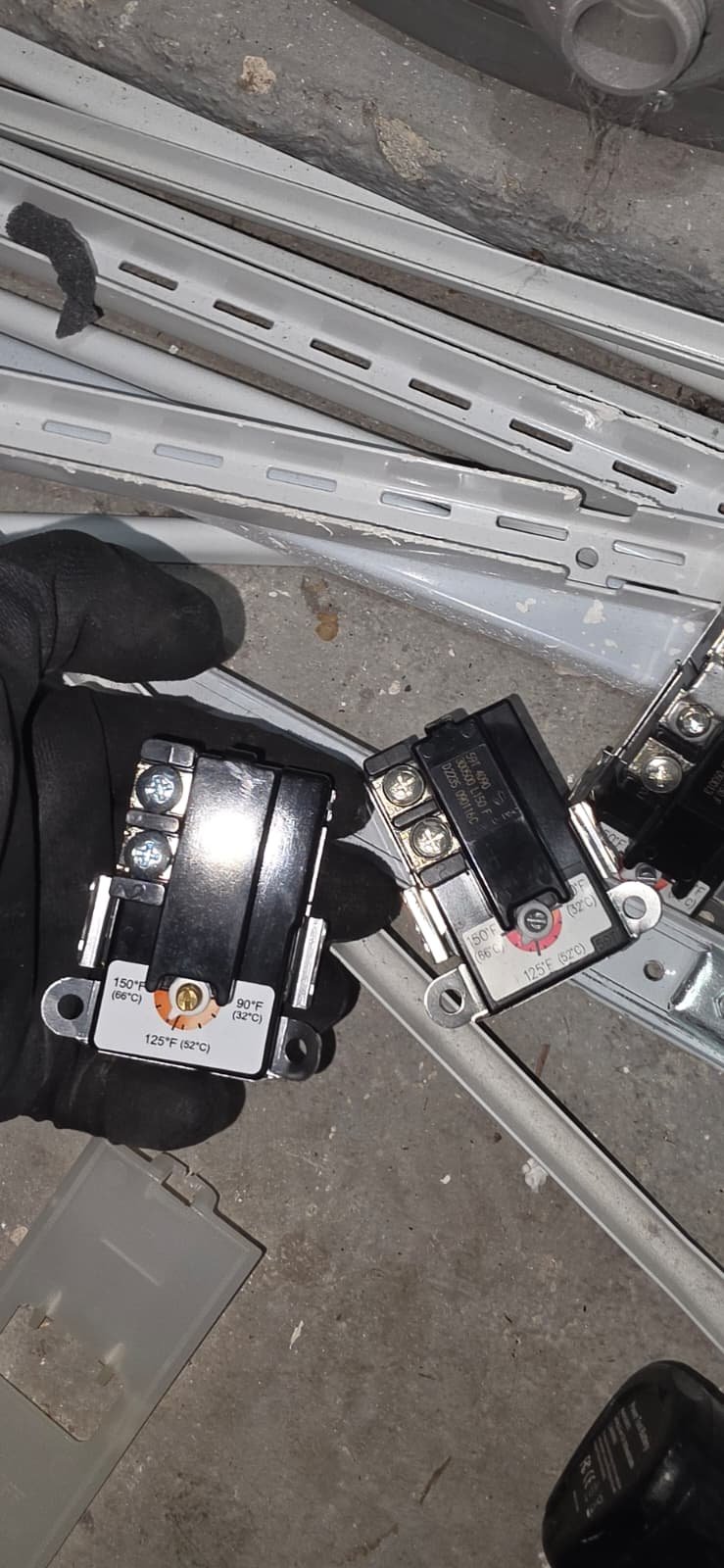 Thermostat Replacement - Tampa, FL 33624 Two thermostats held in a gloved hand on concrete floor in Tampa, FL 33624.