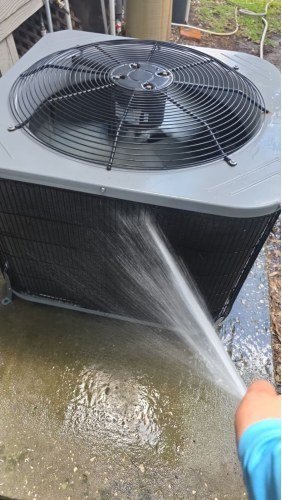 Technician rinsing an outdoor AC condenser coil during a Home Therapy Club tune-up in Tampa